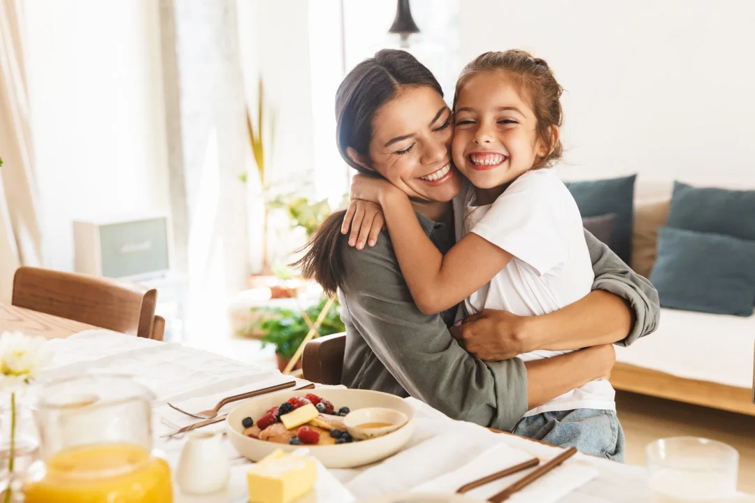 mother and young daughter sitting together hugging at breakfast table