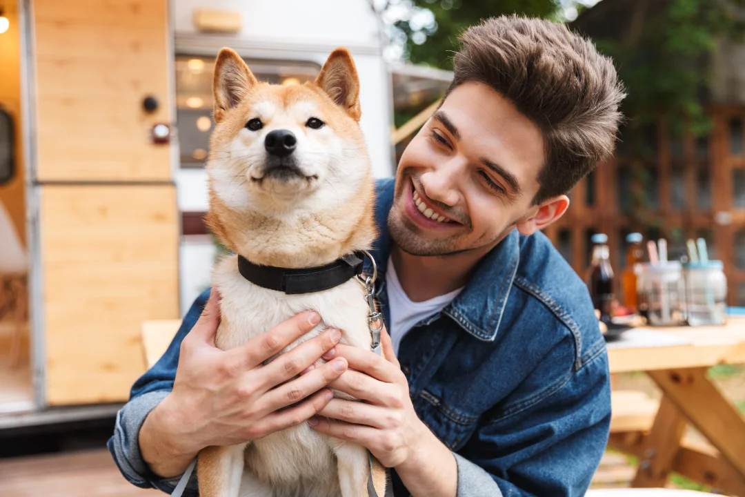 young adult male in jean jacket smiling brightly while holding his pet dog